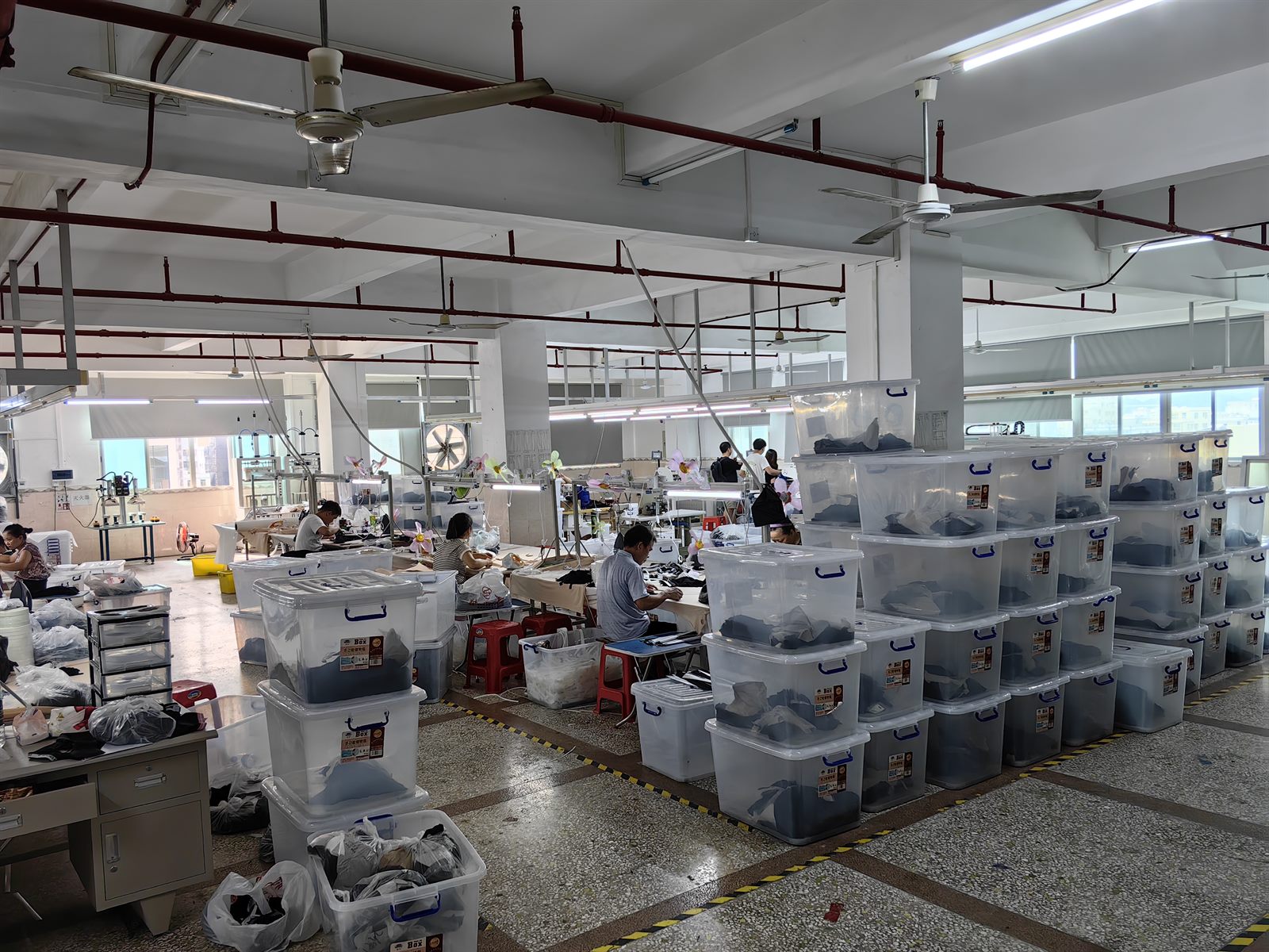 LJVOGUES 车间裁片与半成品周转区实拍：透明周转箱按工序分类码放，箱体贴批次标签